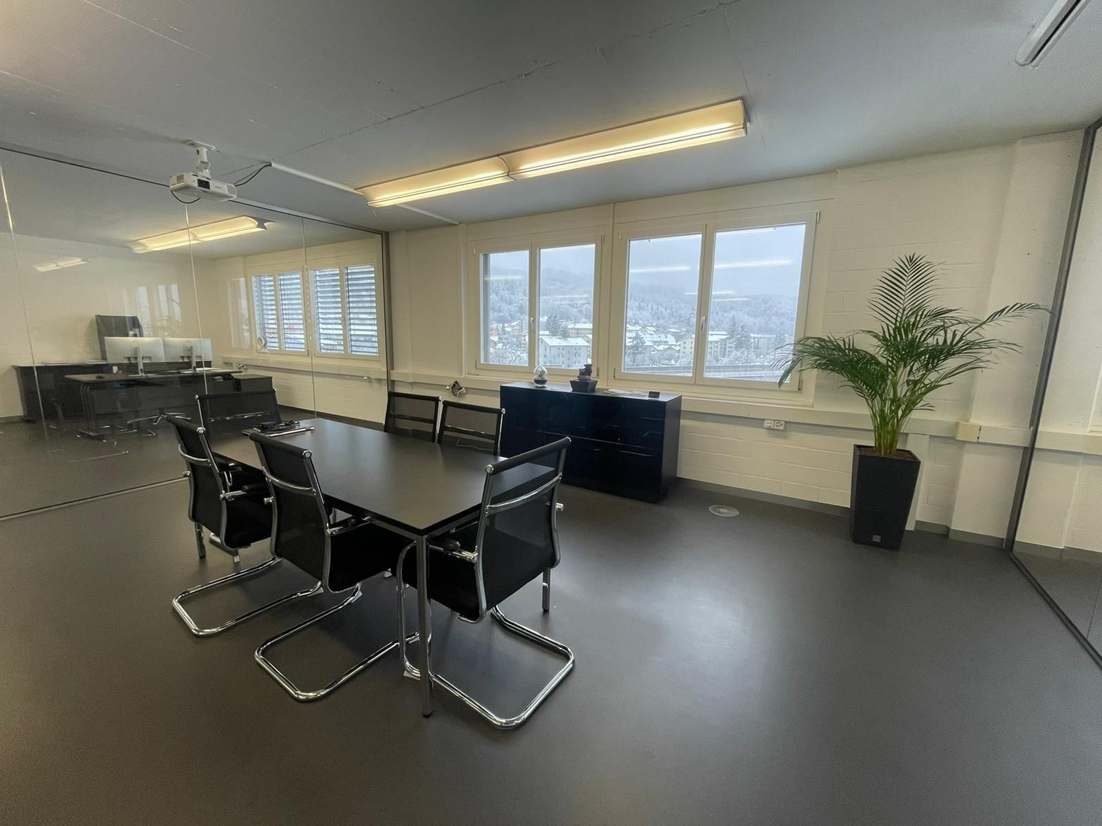 Modern conference room with black table, chairs, projector, and large windows overlooking a cityscape.